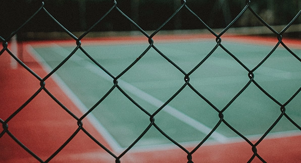 Imagem mostrando uma quadra de tênis cercada por uma tela alambrado revestida em PVC verde